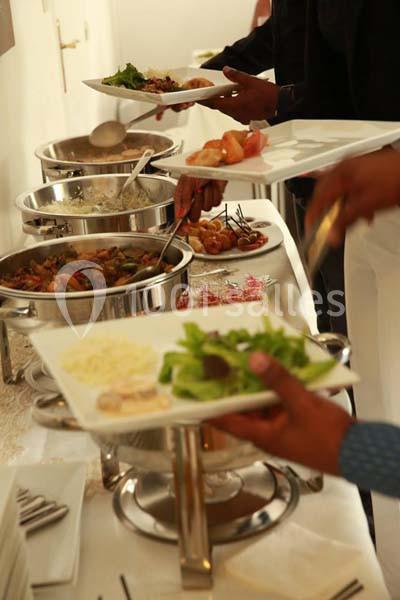 Personnes se servant à un buffet avec des plats variés, incluant des légumes, des sauces et des accompagnements.