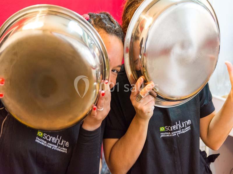 Deux personnes tenant des couvercles métalliques devant leur visage, portant des t-shirts noirs avec un logo visible.