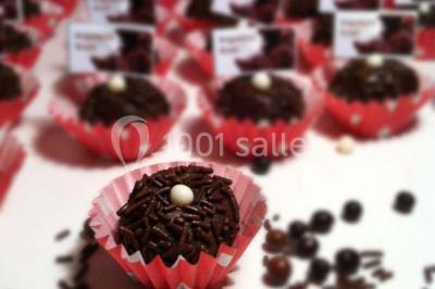 Salle de réception décorée avec des tables alignées, nappes blanches, chaises pliantes et ornements suspendus.