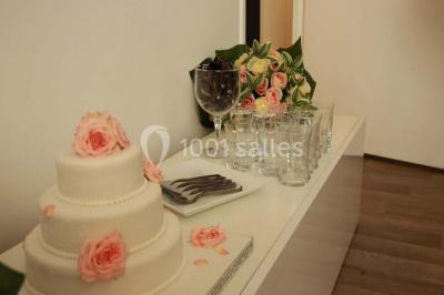 Salle de réception décorée avec des tables alignées, nappes blanches, chaises pliantes et ornements suspendus.