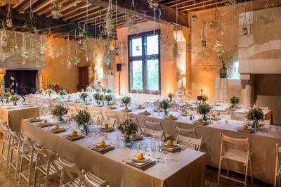 Salle de réception décorée avec des tables alignées, nappes blanches, chaises pliantes et ornements suspendus.