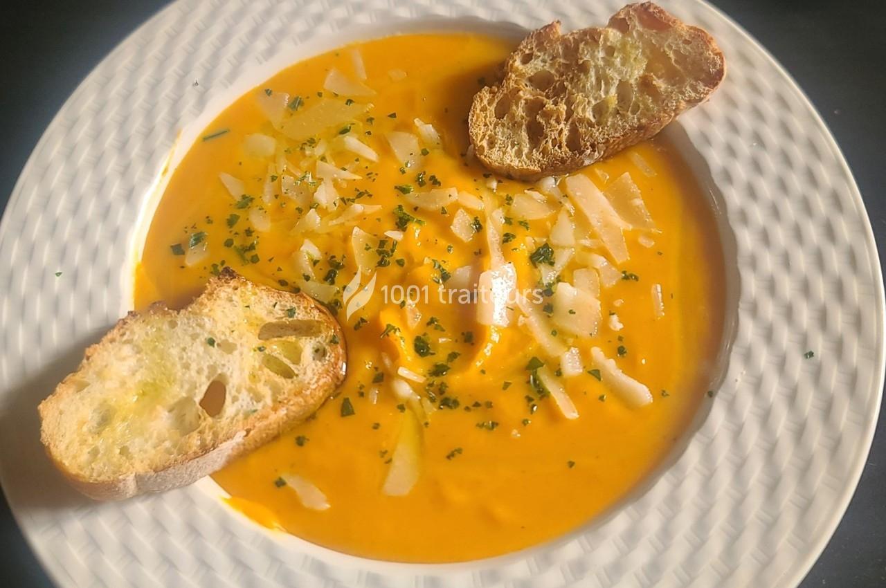 Soupe orange garnie de copeaux de fromage, herbes et accompagnée de deux tranches de pain grillé.