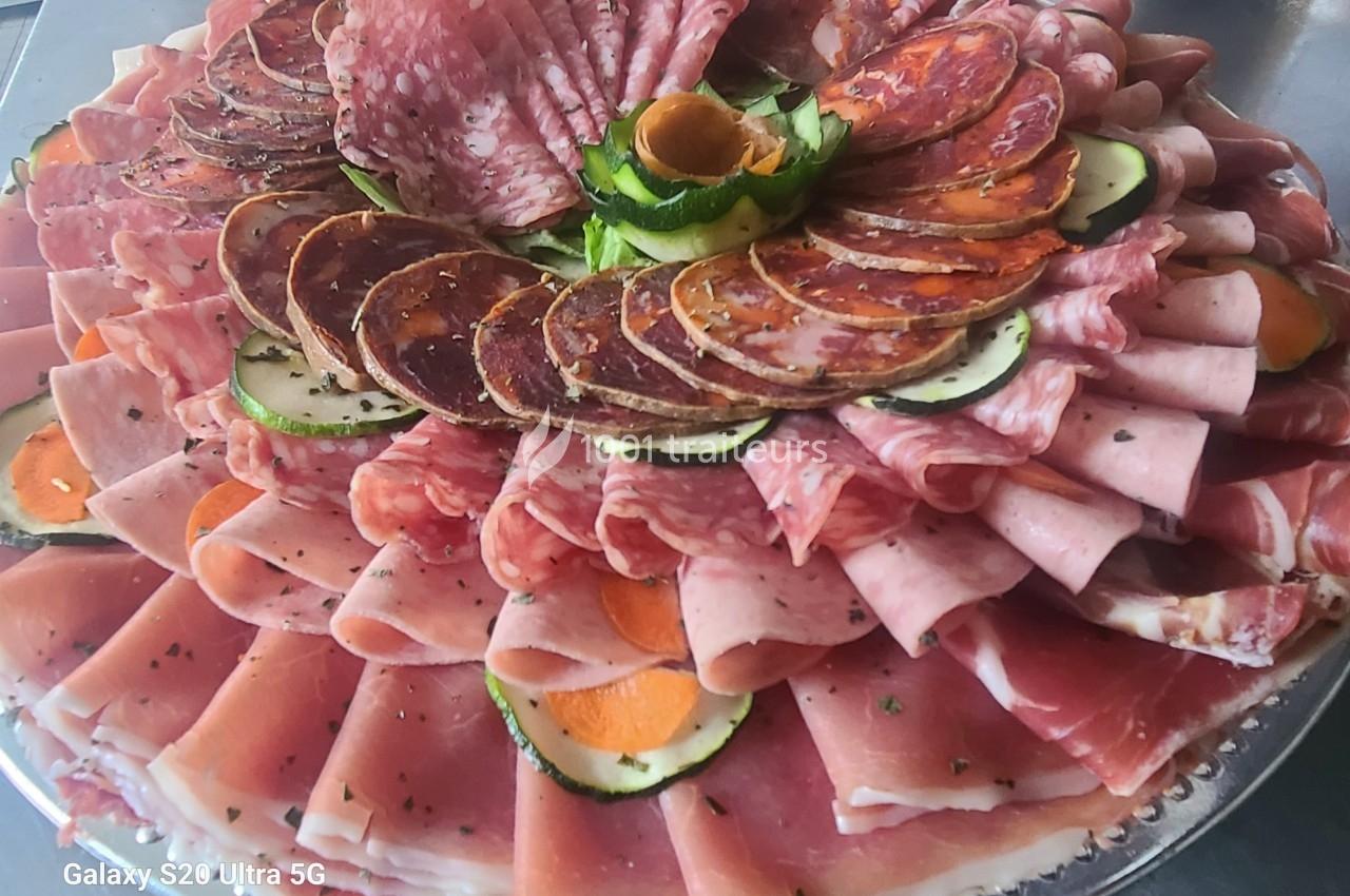 Plateau de charcuterie variée avec jambon, saucisson et décoration de légumes sur un plat argenté.