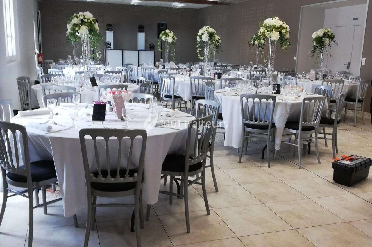 Salle de réception décorée avec des tables rondes, nappes blanches, chaises grises et centres de table fleuris.