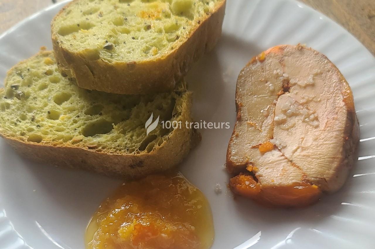 Tranche de foie gras avec confiture d'abricot et pain aux herbes sur une assiette blanche.