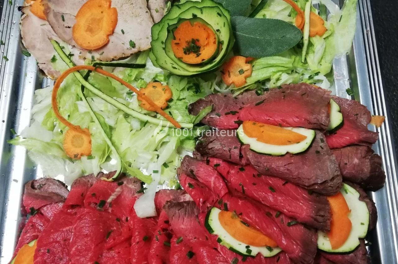 Plateau de viande froide avec tranches de rôti de bœuf et de porc, décoré de légumes frais et herbes.