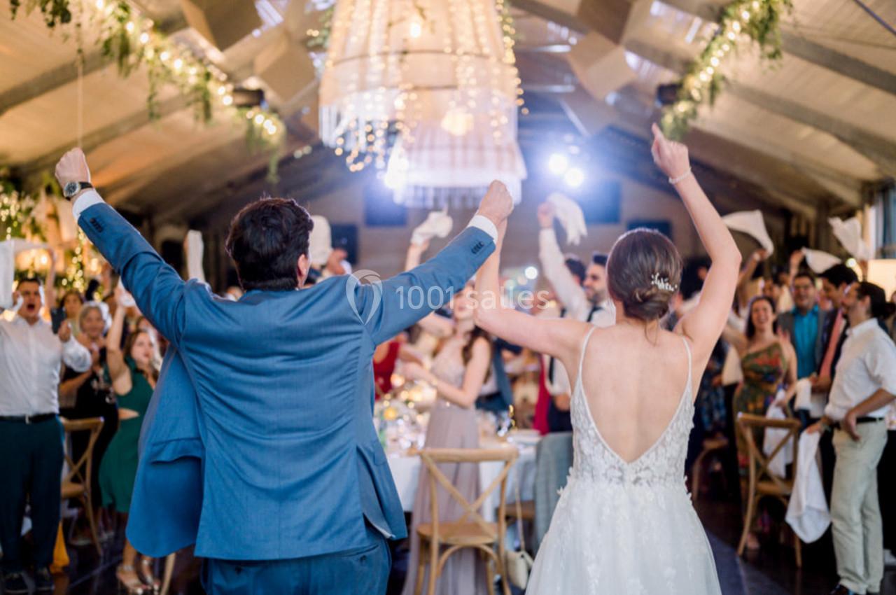 Un couple de mariés danse sous des lumières suspendues, entouré d'invités célébrant avec des serviettes levées.