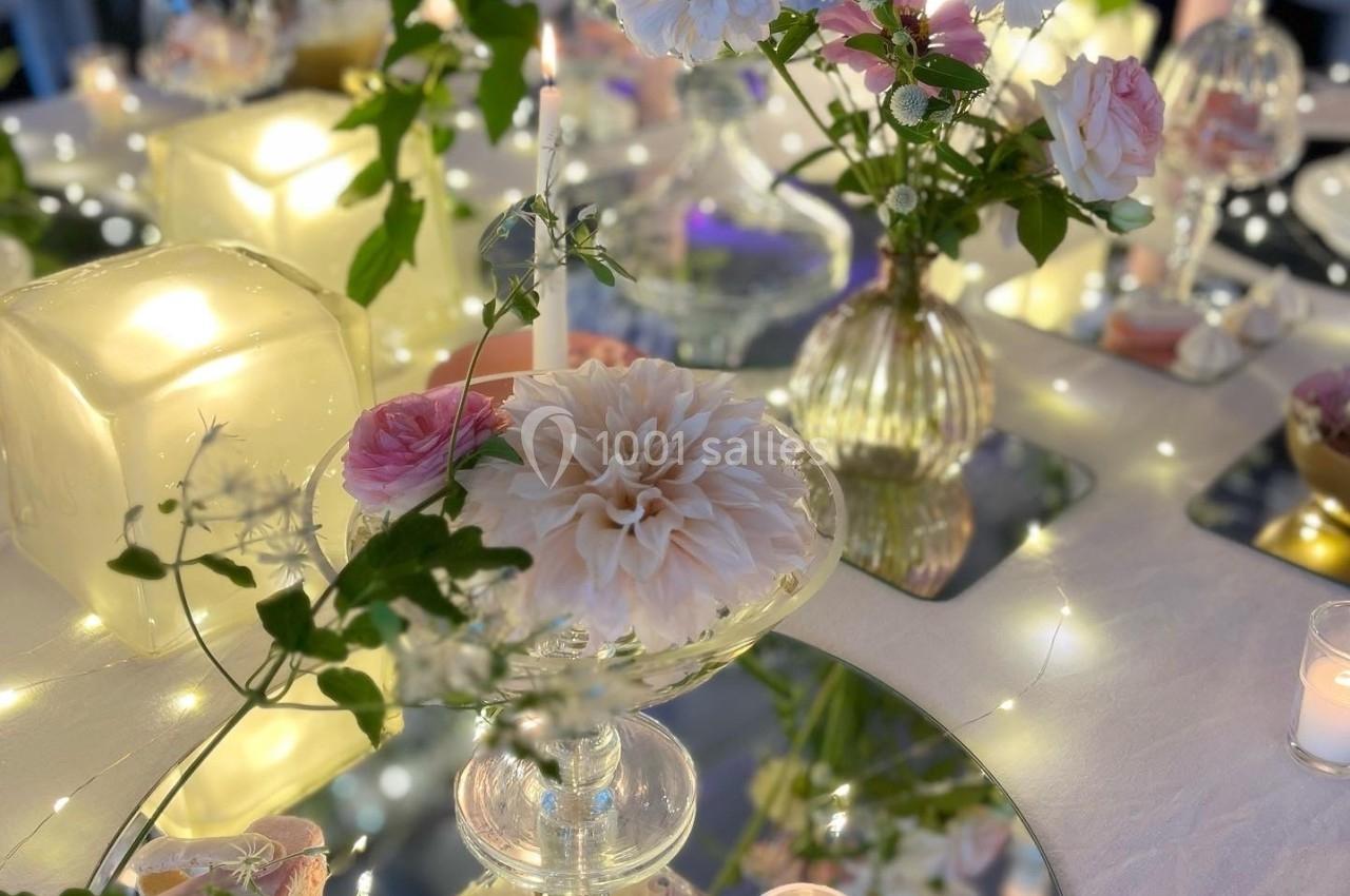 Arrangement floral élégant avec bougies, miroirs et guirlandes lumineuses sur une table décorée.