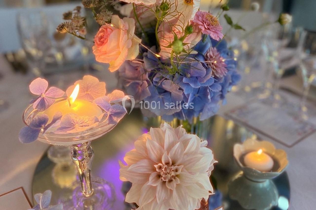Centre de table floral avec dahlias, hortensias et cosmos, bougies allumées et menus disposés sur une table élégante.
