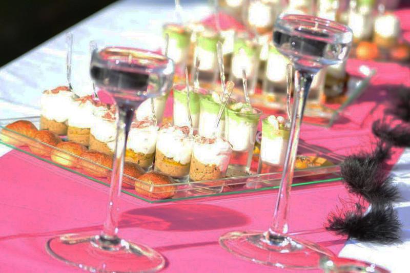 Verres à pied et verrines disposés sur une table décorée de nappes roses et blanches lors d'un événement.