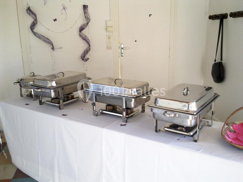 Buffet avec plusieurs plats en inox sur une table blanche, décorée de rubans et d'éléments festifs.