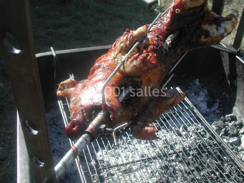Cochon entier rôti à la broche sur un barbecue en plein air, avec des braises visibles en dessous.