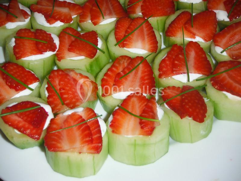 Rondelles de concombre garnies de crème, tranches de fraise et brins de ciboulette, disposées sur une assiette.