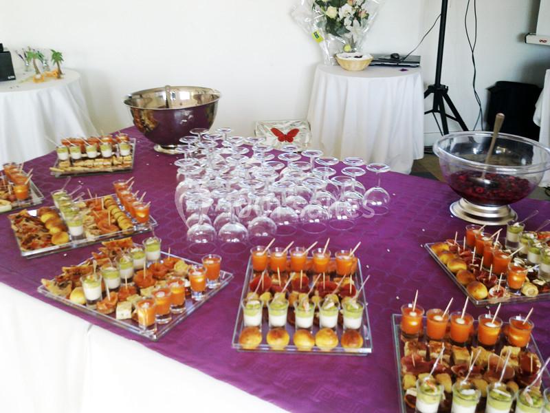Table dressée avec verrines colorées, amuse-bouches variés, verres à pied et saladier sur une nappe violette.