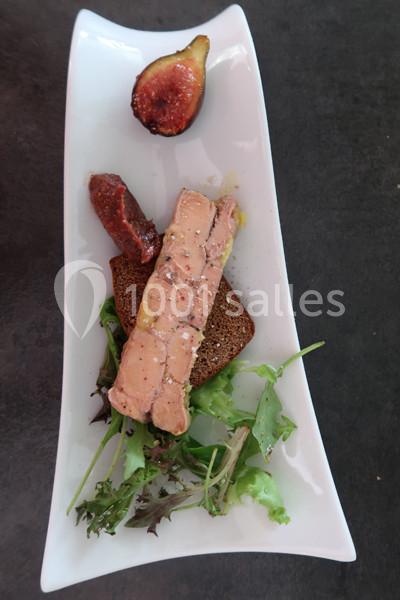 Tranche de foie gras sur pain, accompagnée de salade, figue fraîche et chutney, présentée sur une assiette blanche.