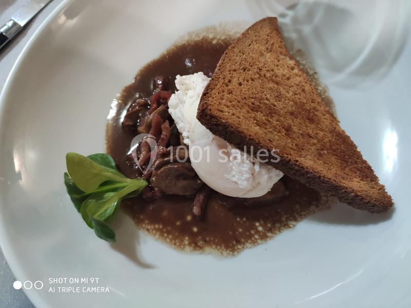 Assiette contenant un œuf poché, des champignons, des lardons, une tranche de pain grillé et une garniture de mâche.