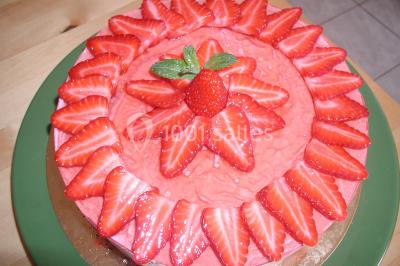 Gâteau décoré de tranches de fraises disposées en cercle avec une fraise entière et une feuille de menthe au centre.