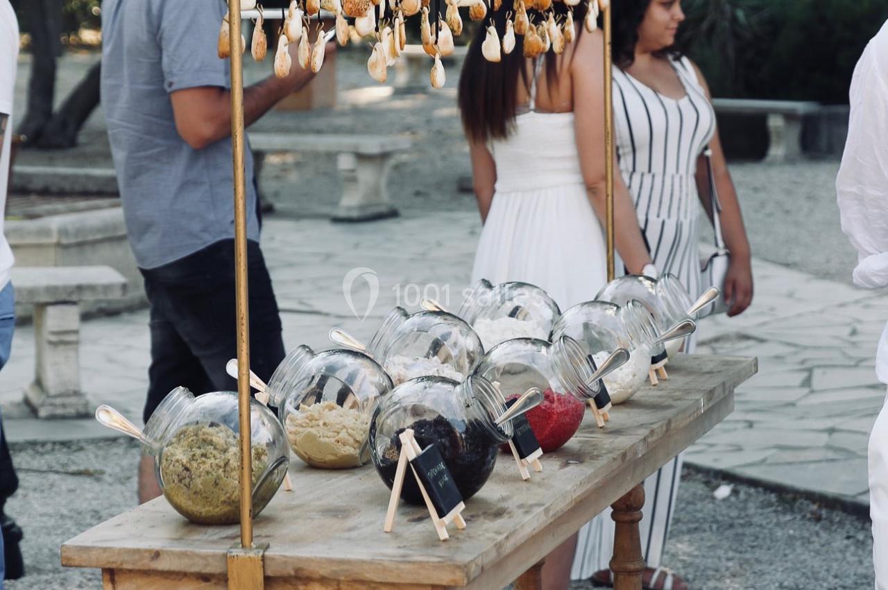 Stand en bois avec des bocaux d'épices et des décorations suspendues, situé en extérieur avec des personnes en arrière-plan.