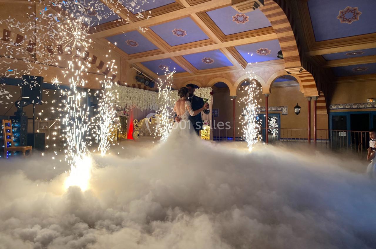 Un couple danse au milieu d'une salle décorée, entouré de fumée, d'étincelles et d'un éclairage chaleureux.