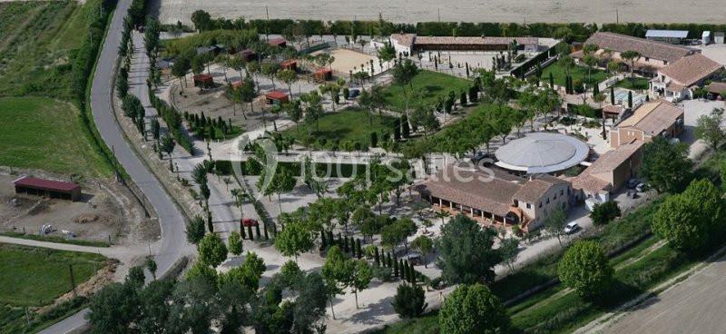 Vue aérienne d'un domaine rural avec bâtiments, espaces verts, routes et installations extérieures.