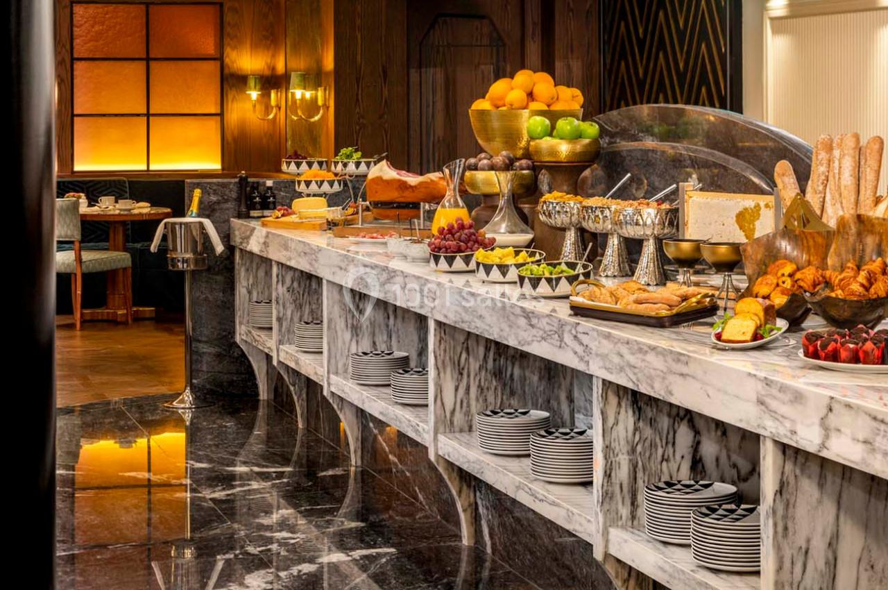 Buffet avec fruits, viennoiseries, pains, charcuterie et plats variés sur un comptoir en marbre dans une salle élégante.