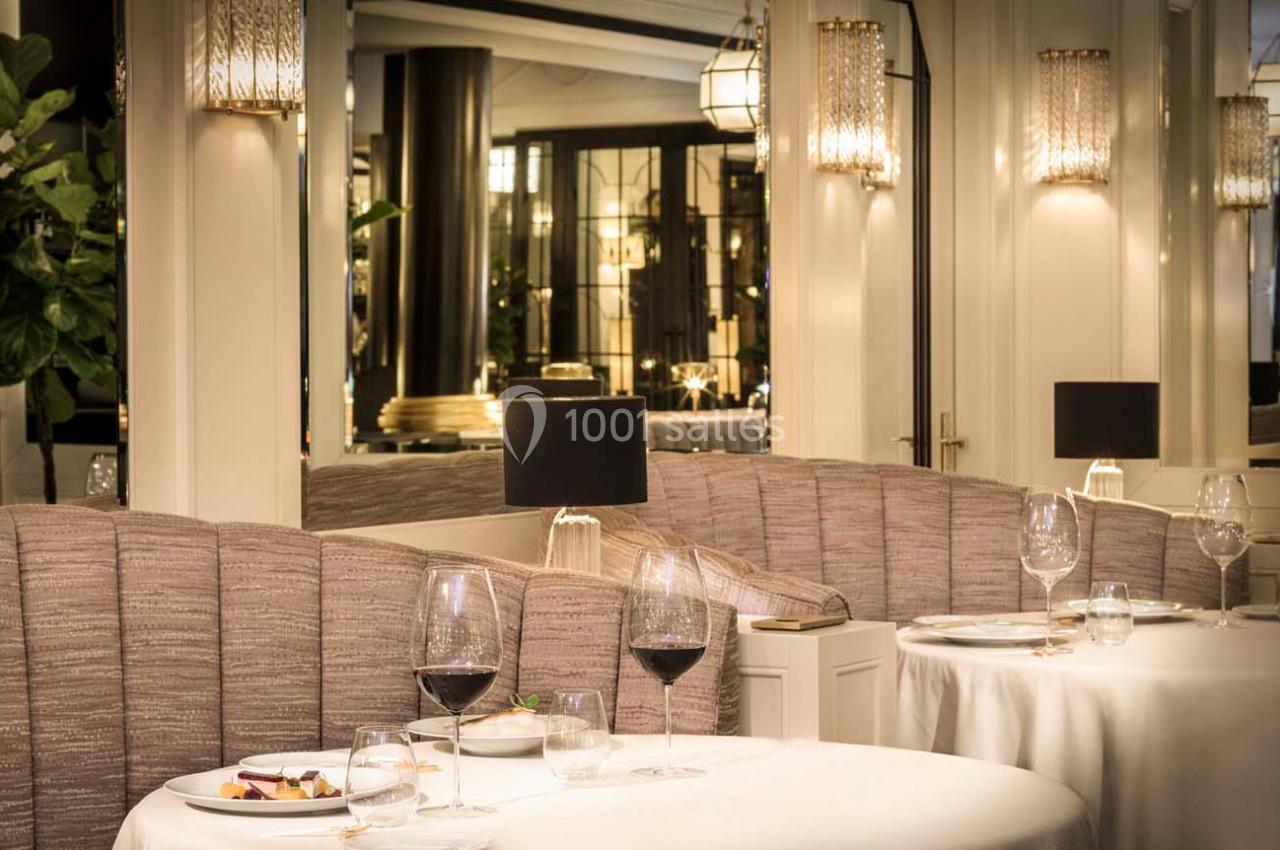 Salle de restaurant élégante avec tables dressées, banquettes en tissu, verres à vin et éclairage chaleureux.