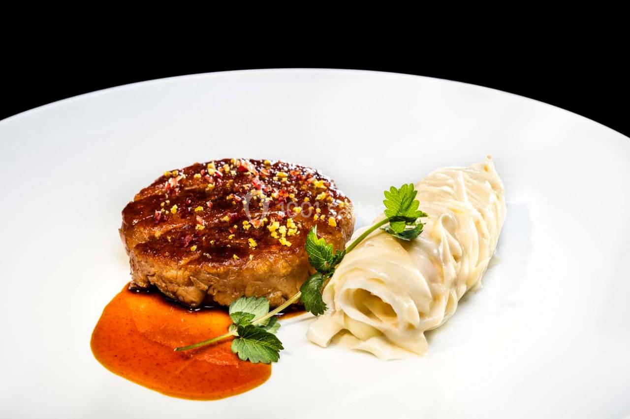 Assiette avec un steak végétal nappé de sauce, accompagné de tagliatelles et décoré de feuilles de persil.