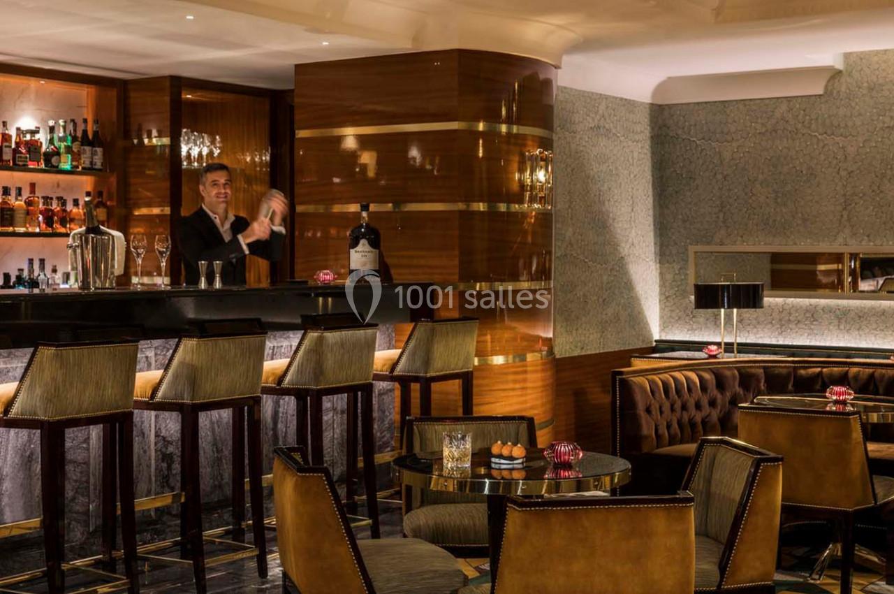 Un barman prépare un cocktail derrière un comptoir dans un bar élégant avec des tables et des fauteuils en cuir.