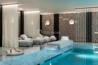 Salle de soins avec table de massage, produits de beauté, serviettes pliées, plantes et éclairage tamisé.