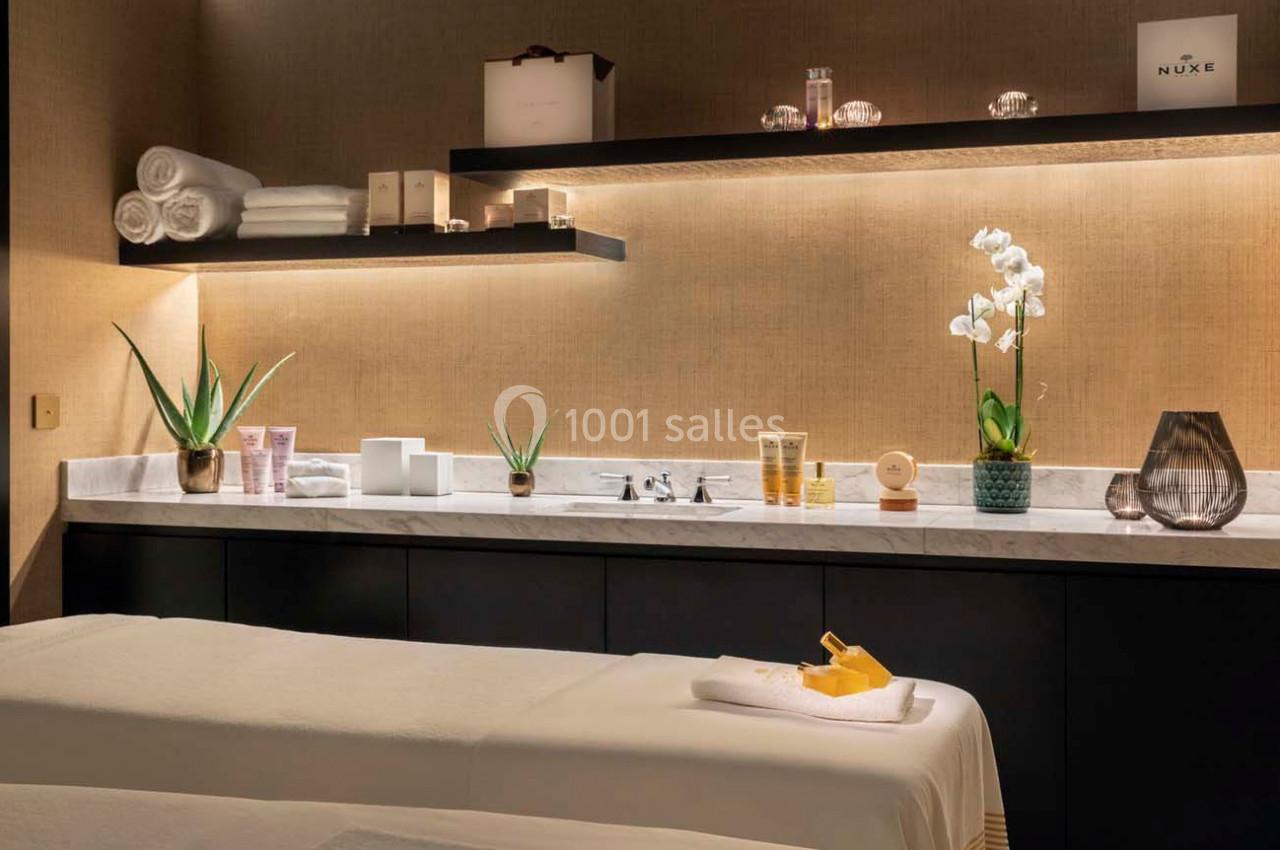 Salle de soins avec table de massage, produits de beauté, serviettes pliées, plantes et éclairage tamisé.
