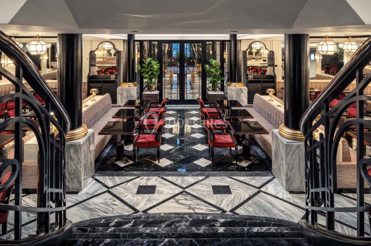 Salle de restaurant élégante avec tables noires, chaises rouges, sol en marbre et décoration raffinée.