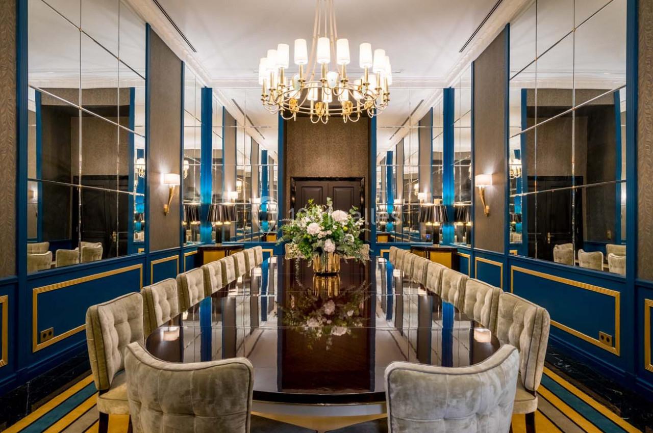 Salle à manger élégante avec une grande table en bois, des chaises rembourrées, des miroirs et un lustre central.