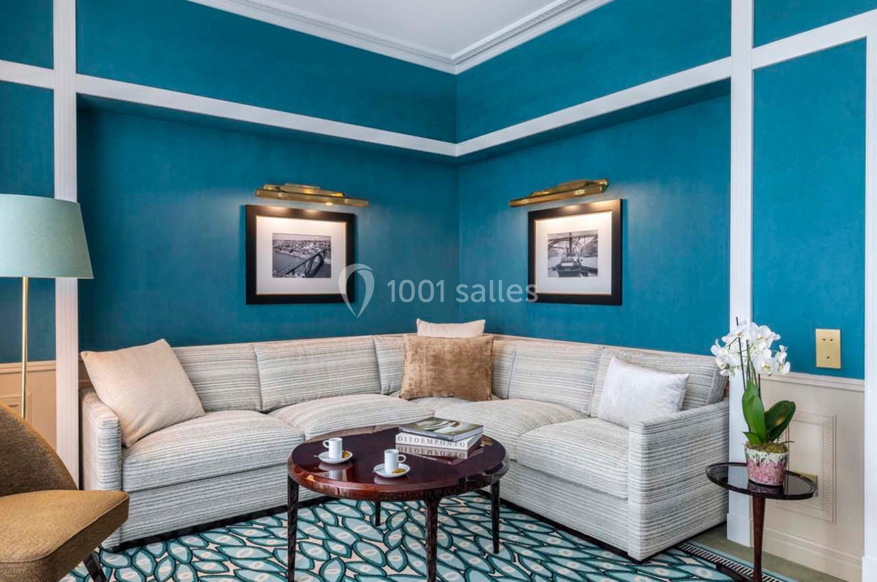 Salon avec canapé d'angle beige, murs bleus, table basse ronde avec tasses et orchidée sur une table d'appoint.