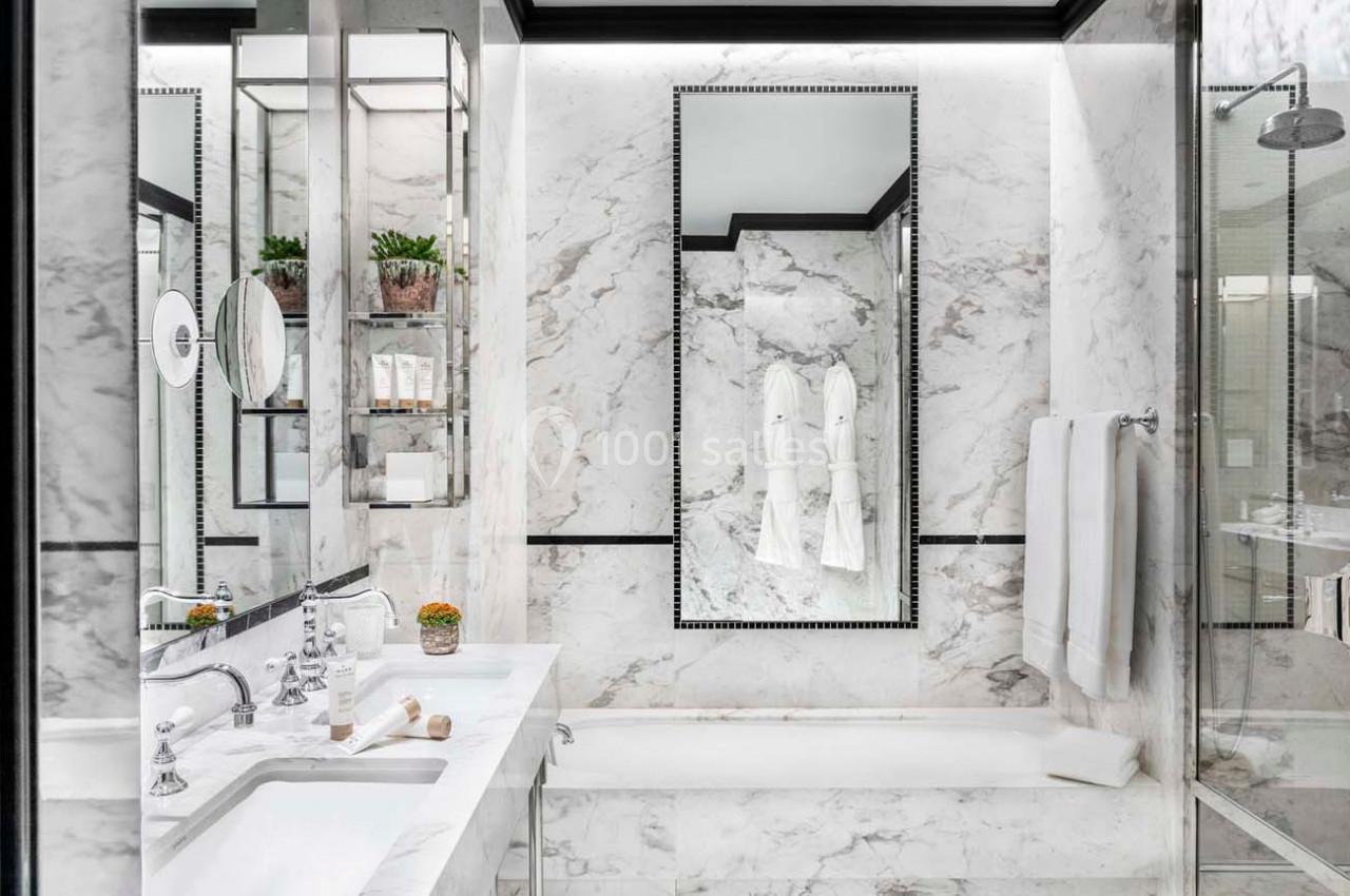 Salle de bain luxueuse avec murs en marbre, miroir encadré, baignoire, lavabo moderne et serviettes blanches.