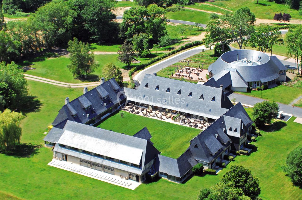 Vue aérienne d'un complexe architectural en forme de U avec un bâtiment circulaire adjacent, entouré de verdure.