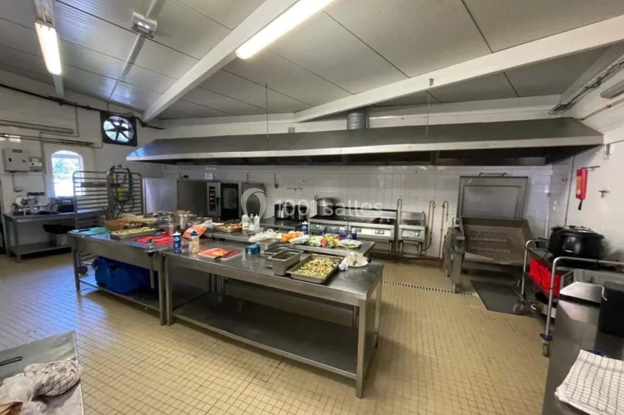 Cuisine professionnelle équipée avec plans de travail en inox, appareils de cuisson et ustensiles disposés.