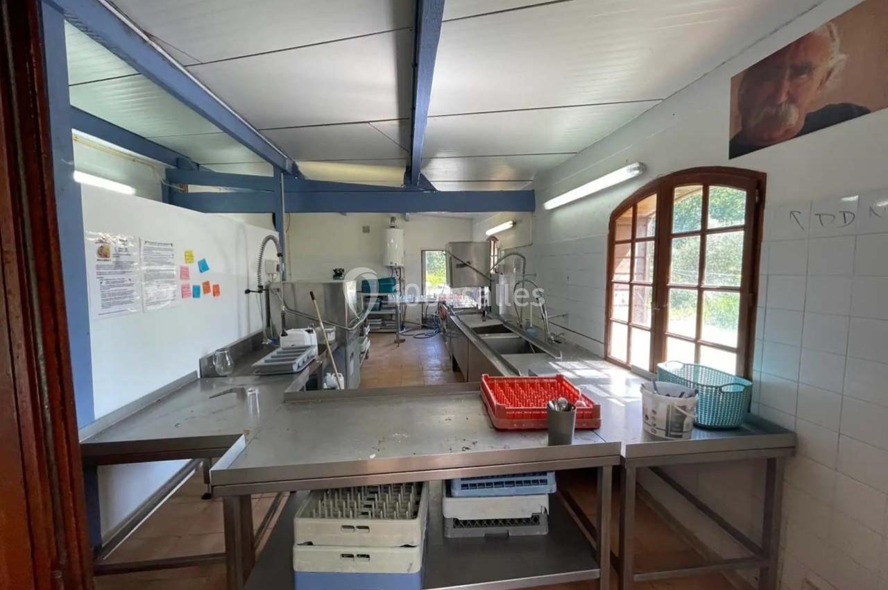 Cuisine collective équipée de plans de travail en inox, éviers, paniers de vaisselle et éclairée par une fenêtre.