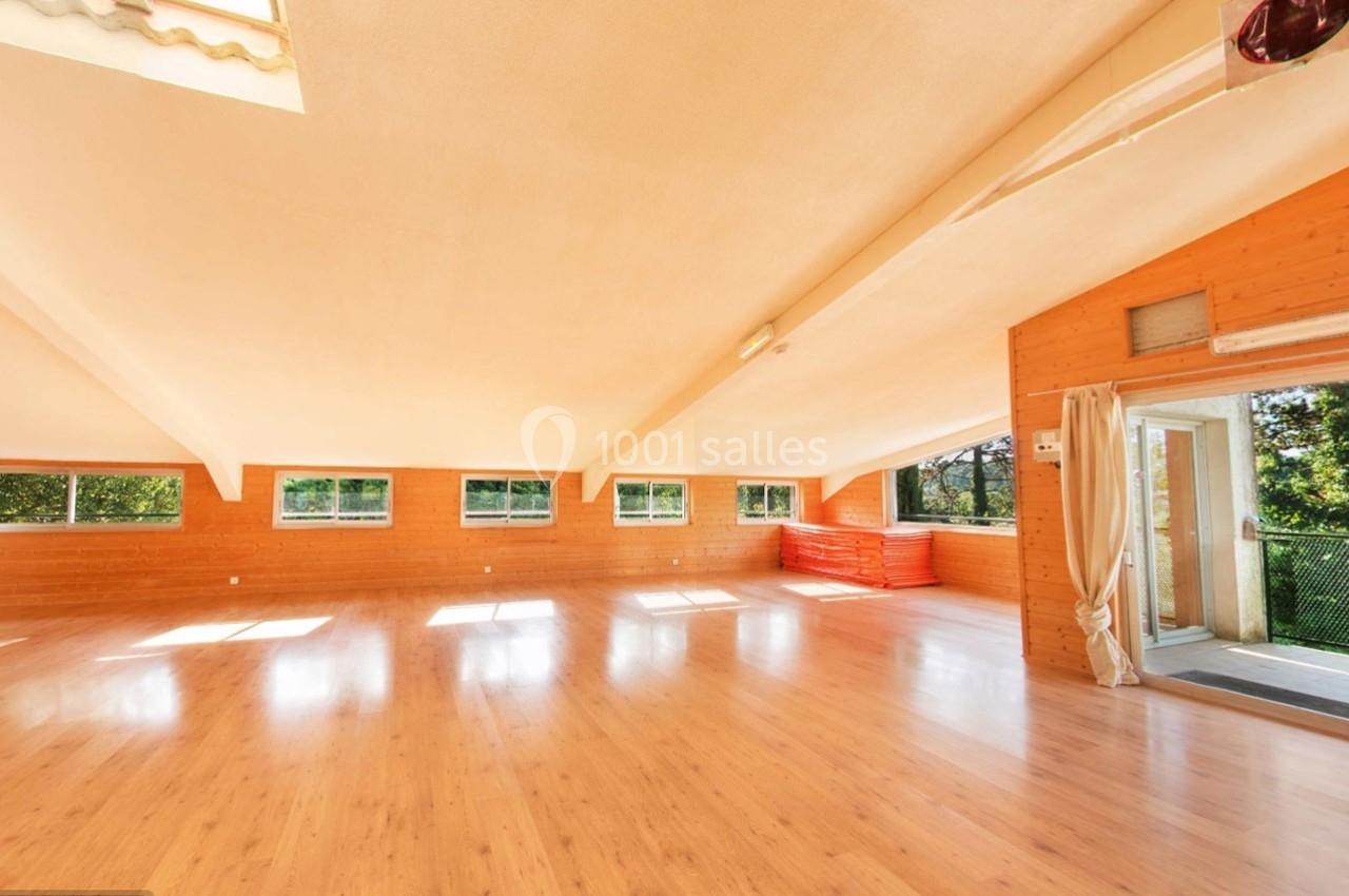 Salle spacieuse avec parquet clair, murs en bois, grandes fenêtres et lumière naturelle, donnant sur un espace extérieur.