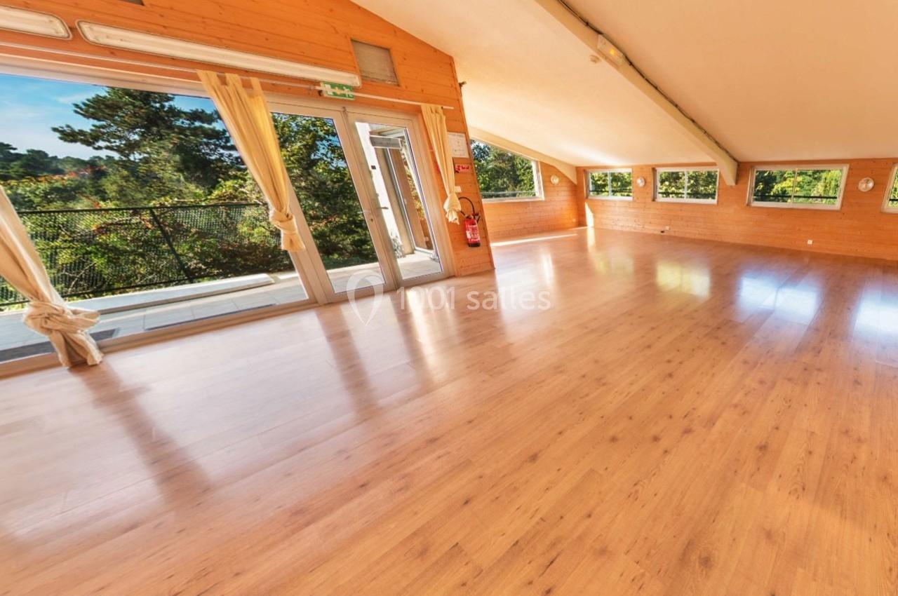 Salle lumineuse avec parquet en bois, grandes fenêtres et vue sur un espace extérieur arboré.