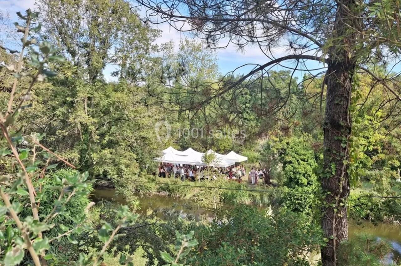 Tentes blanches installées près d'une rivière entourée de végétation et d'arbres sous un ciel dégagé.