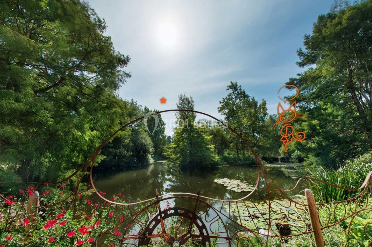 Vue d’un étang entouré de végétation luxuriante, avec une barrière décorative en fer forgé au premier plan.