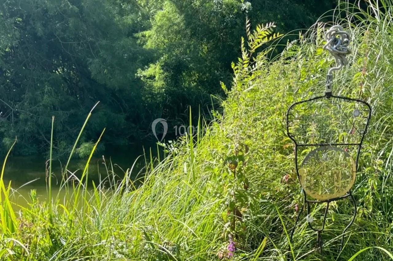 Un piège à poissons suspendu au bord d'une rivière entourée de végétation dense et verdoyante.