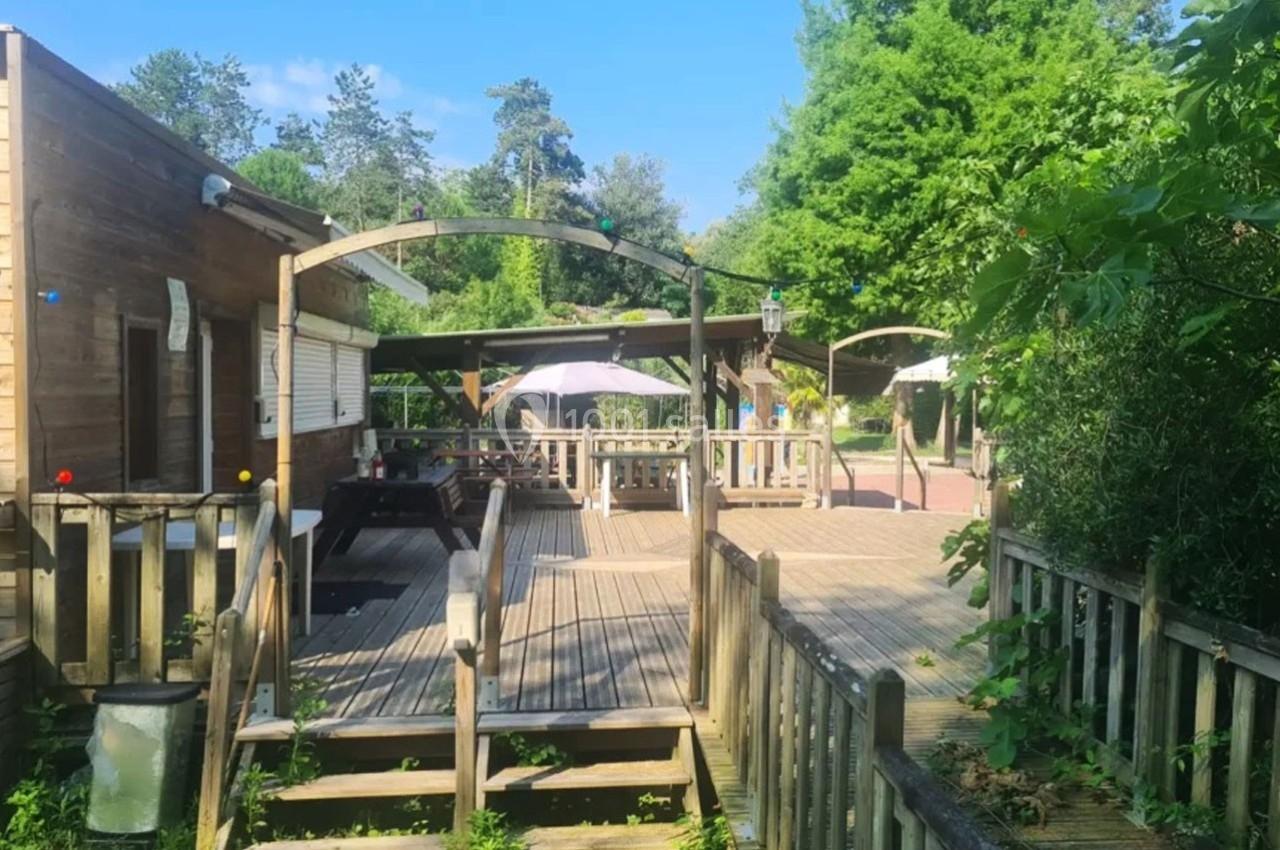 Terrasse en bois avec tables, parasols et pergolas, entourée de verdure et accessible par une rampe.