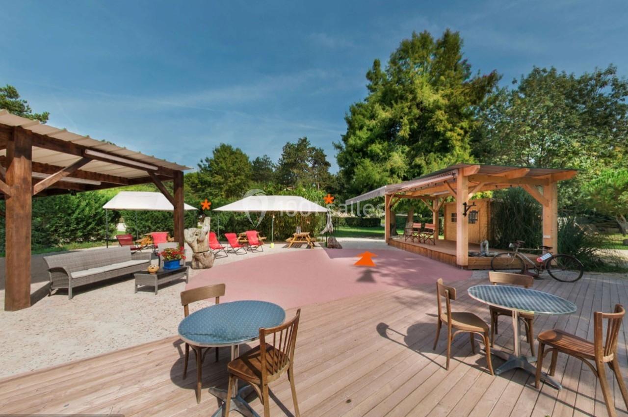 Terrasse extérieure avec tables, chaises, parasols, pergola en bois et végétation en arrière-plan.