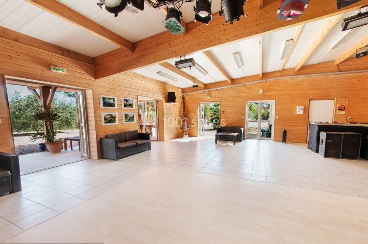 Salle lumineuse avec parquet clair, murs en bois, canapés, baies vitrées donnant sur un extérieur arboré.