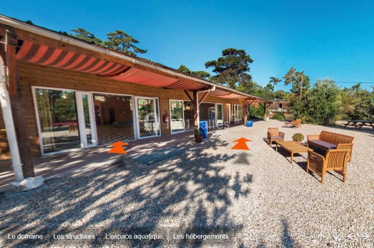 Terrasse en gravier avec mobilier d'extérieur devant un bâtiment en bois, entouré de végétation sous un ciel dégagé.