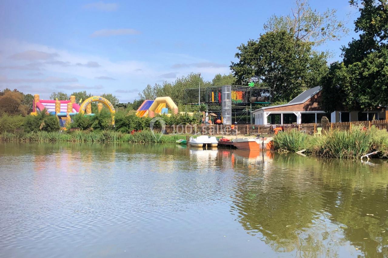 Plan d'eau bordé de végétation avec des structures gonflables colorées et une petite maison en arrière-plan.