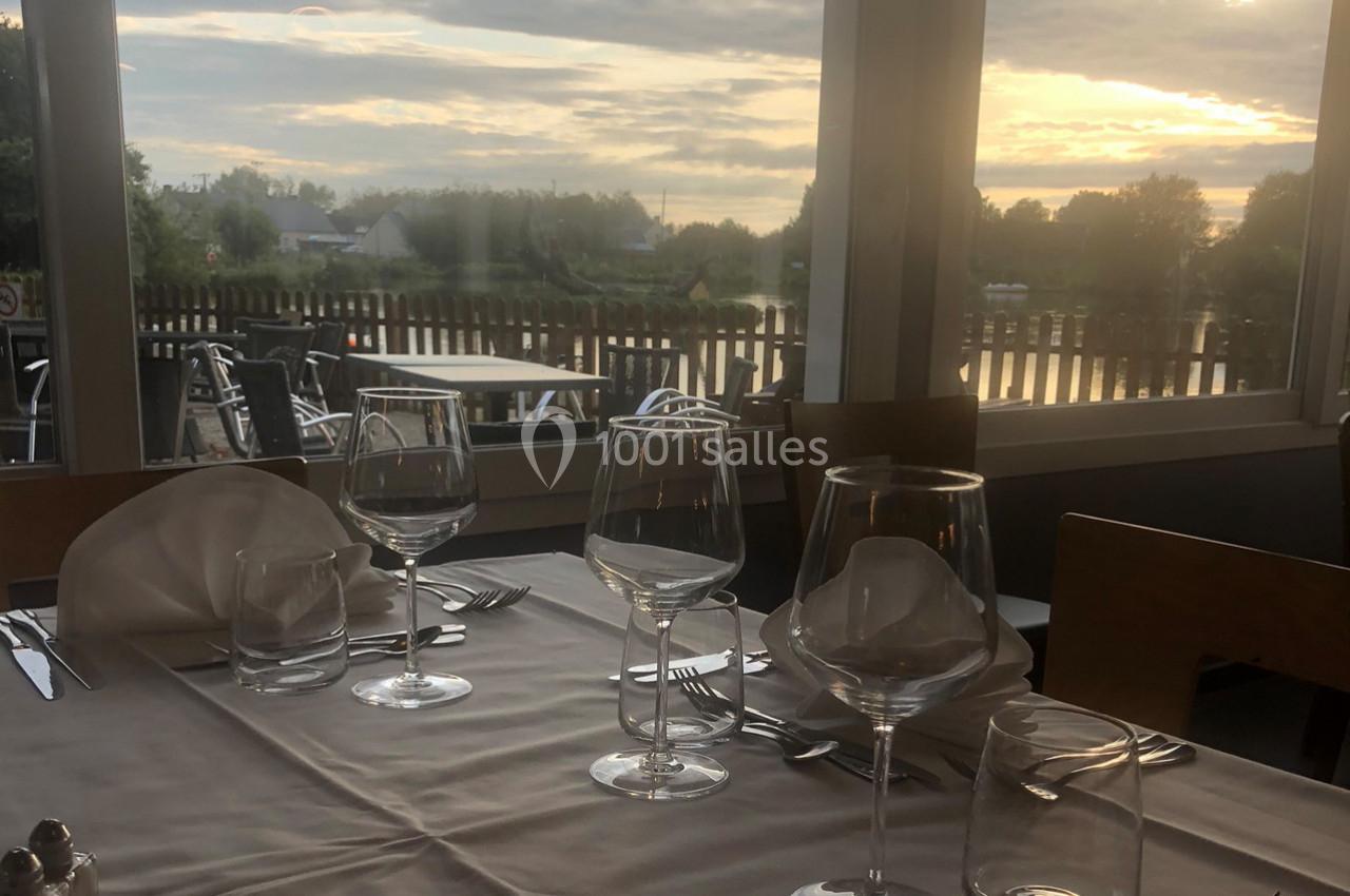Table dressée avec des verres et couverts, vue sur une terrasse et un paysage extérieur au coucher du soleil.