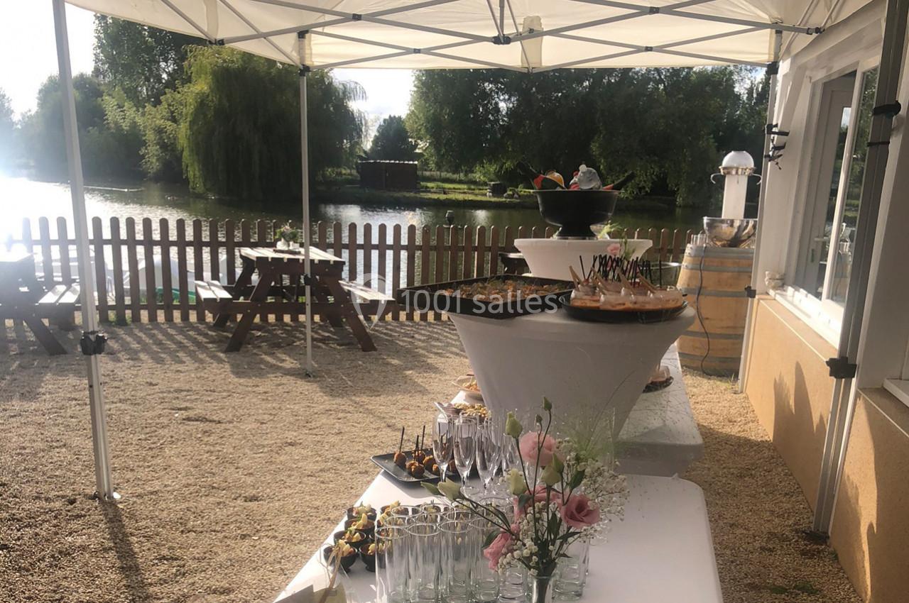 Buffet en plein air sous des tonnelles blanches, avec vue sur un étang et des tables de pique-nique en arrière-plan.