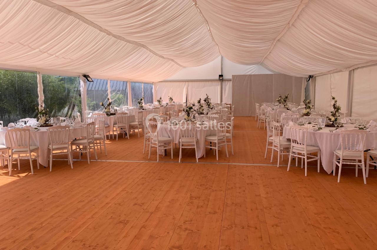 Intérieur d'une tente de réception avec tables rondes dressées, nappes blanches et chaises alignées sur un sol en bois.